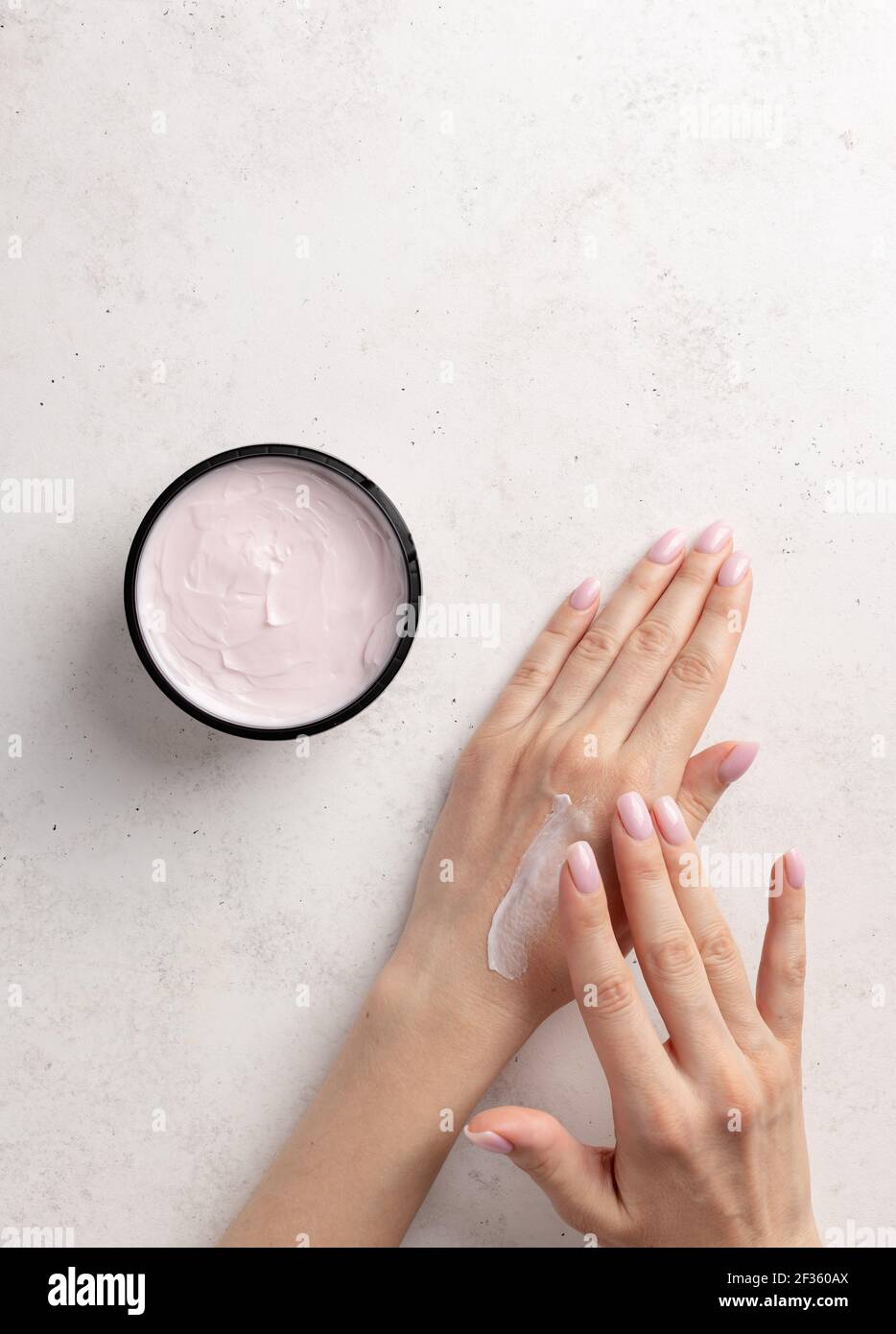 donna spalma le mani crema idratante. Sfondo in pietra bianca. Concetto di cura della pelle. Immagine verticale. Vista dall'alto. Spazio di copia Foto Stock