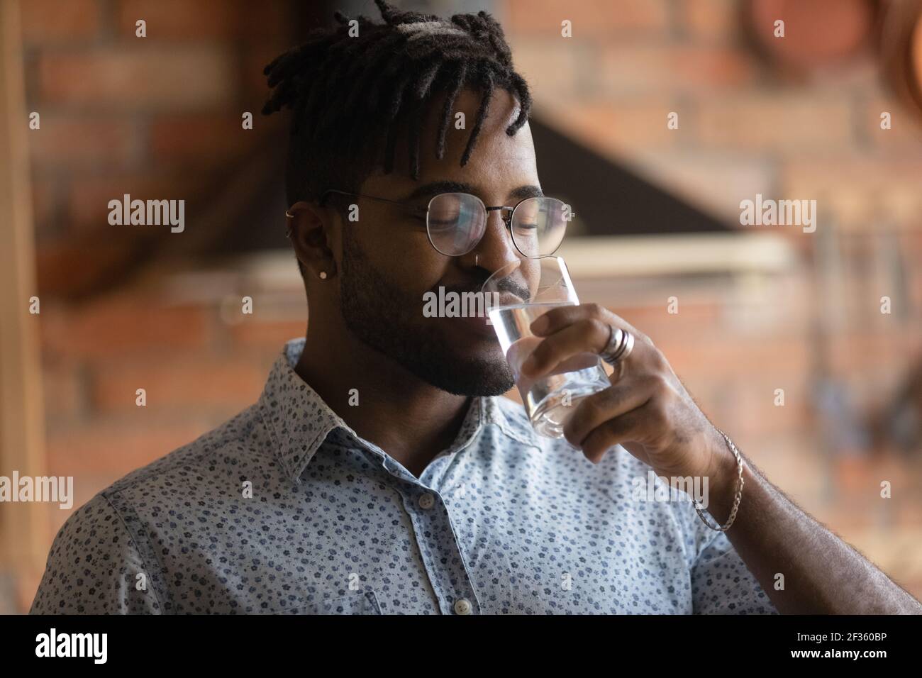 Assetato giovane afro americano uomo bere acqua minerale da vetro Foto Stock