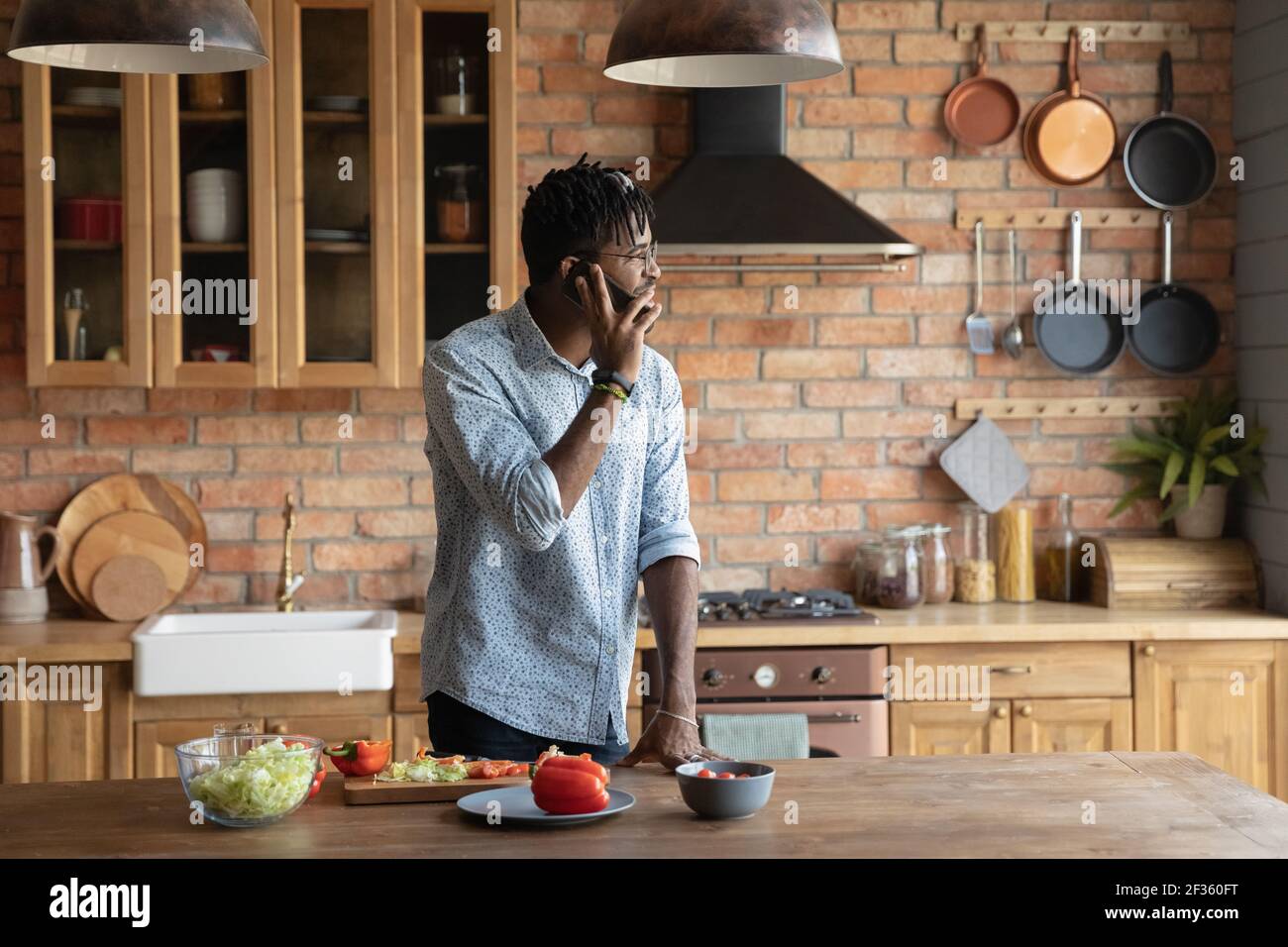 Sorridente hipster maschio nero millenario cucina cibo rispondere telefono chiamata Foto Stock