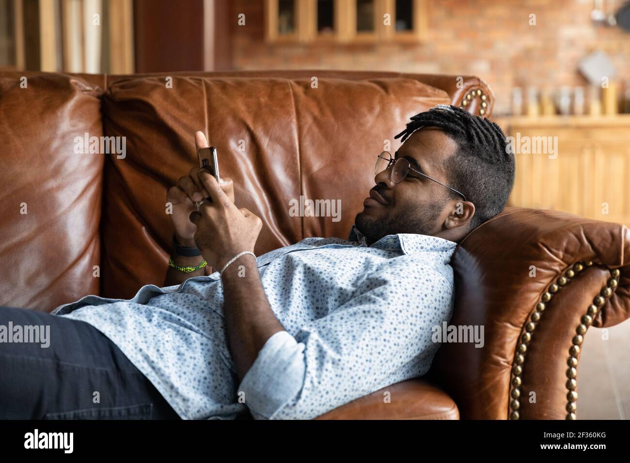 Hipster nero pacifico millennial del tipo sdraiato sul divano usando il telefono Foto Stock