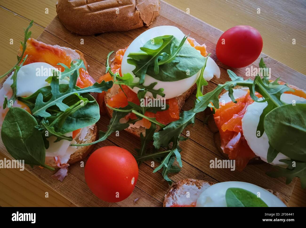 Uova in camicia su toast alla griglia con salmone affumicato, rucola e verdure su tavola bianca. Colazione sana Foto Stock