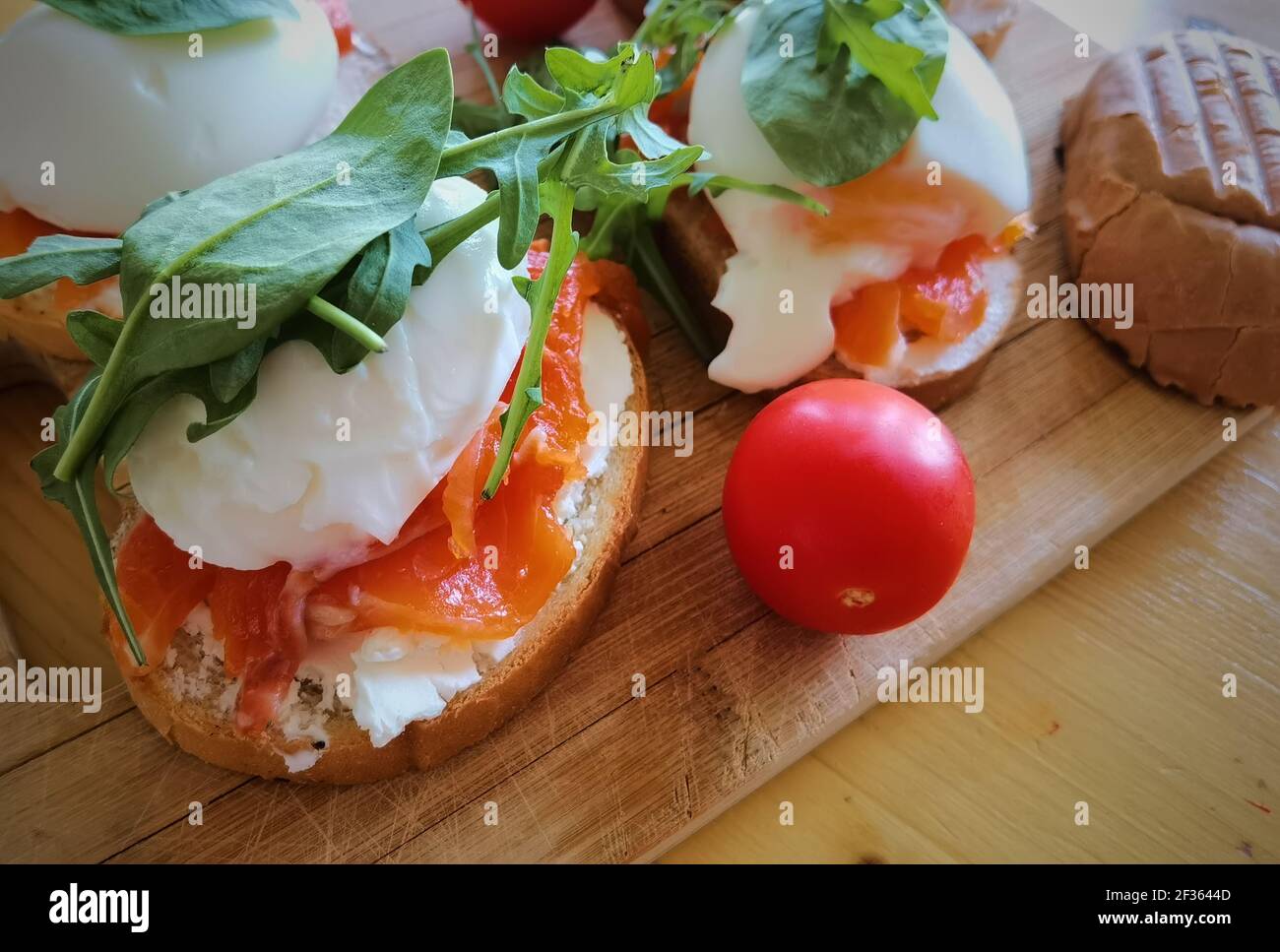 Uova in camicia su toast alla griglia con salmone affumicato, rucola e verdure su tavola bianca. Colazione sana Foto Stock
