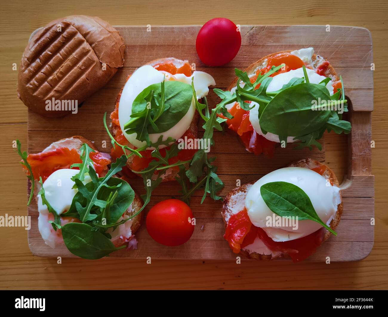 Uova in camicia su toast alla griglia con salmone affumicato, rucola e verdure su tavola bianca. Colazione sana Foto Stock