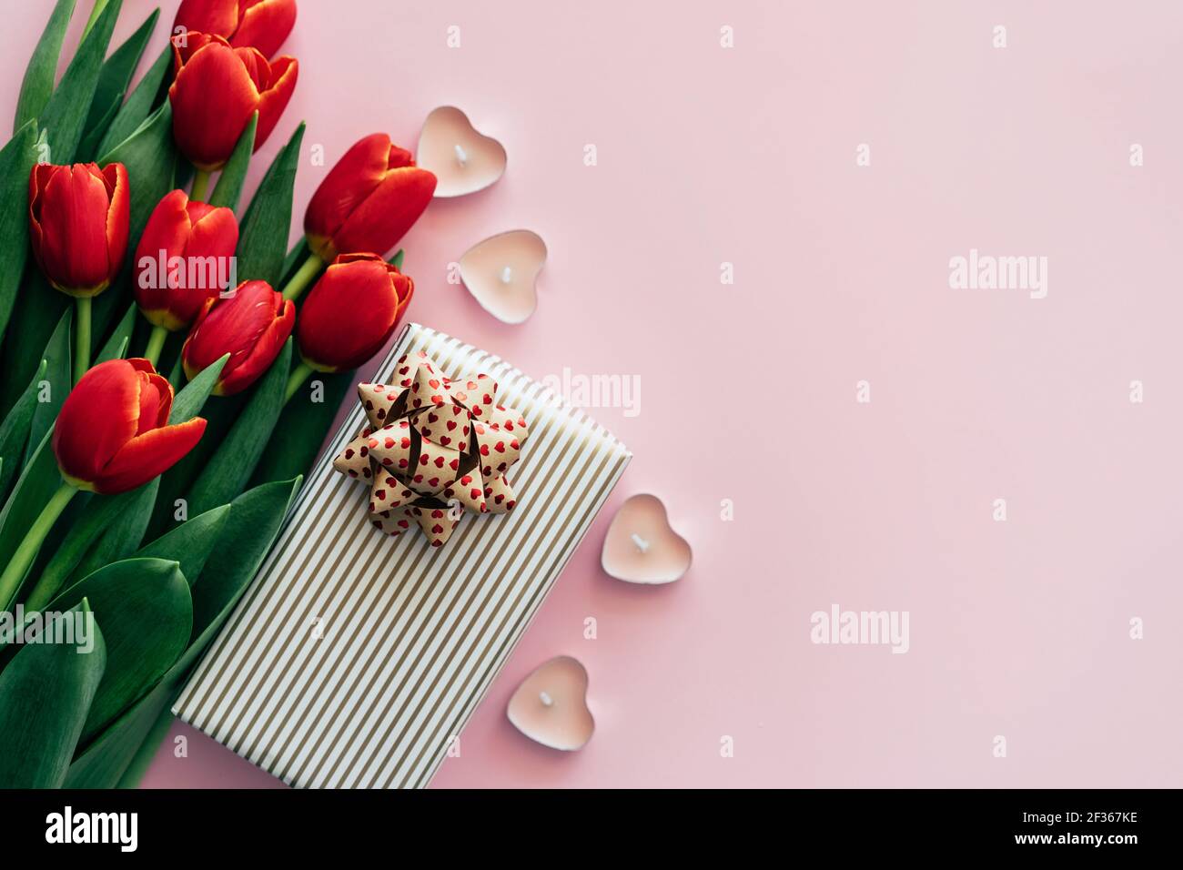 Sfondo rosa con posto per il testo con tulipani rossi fiori freschi confezione regalo e candele a forma di cuore. Foto Stock