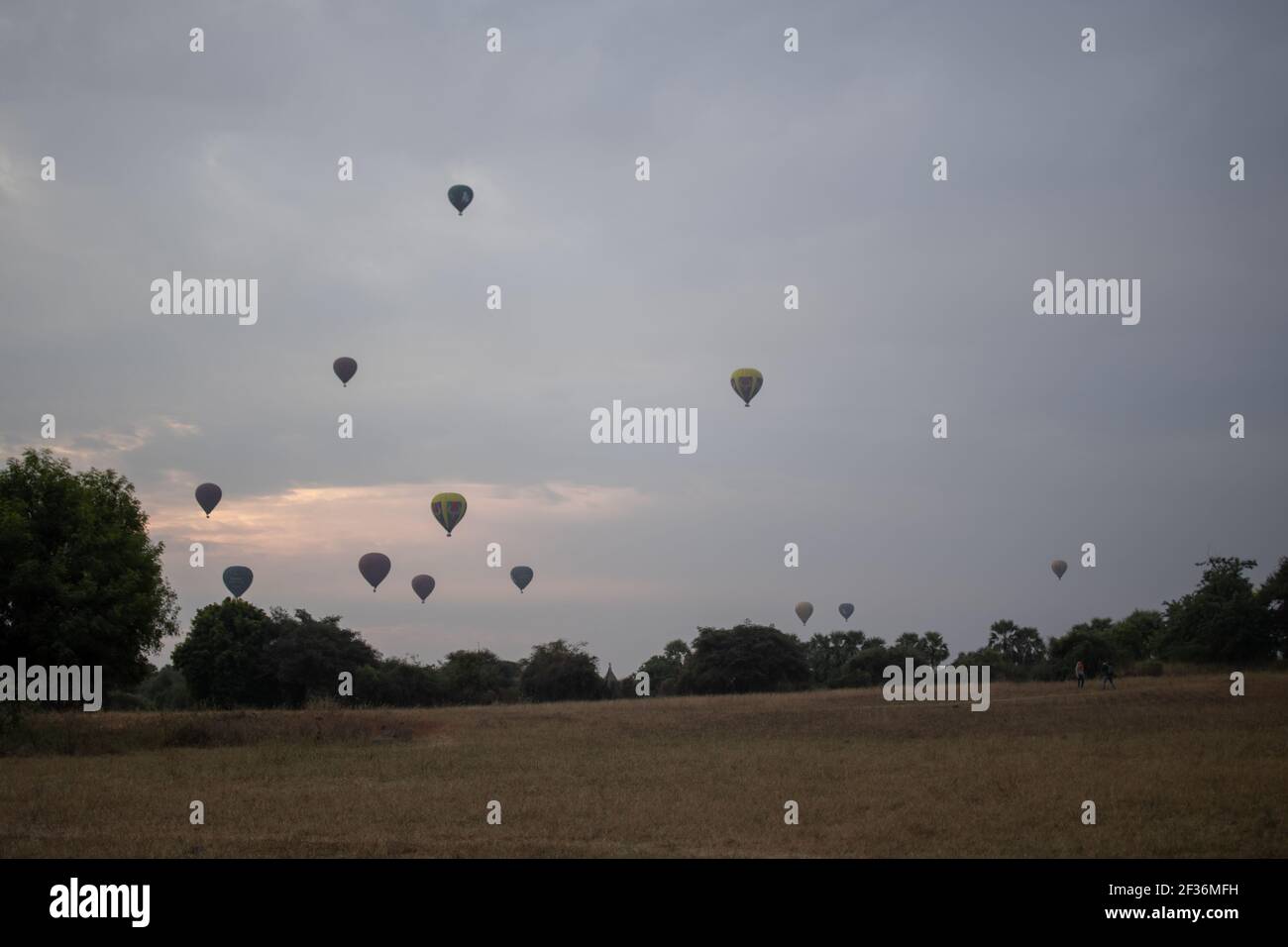 BAGAN, NYAUNG-U, MYANMAR - 2 GENNAIO 2020: Due turisti guardano i mongolfiera nel cielo durante la mattina presto in una giornata nuvolosa da un campo Foto Stock