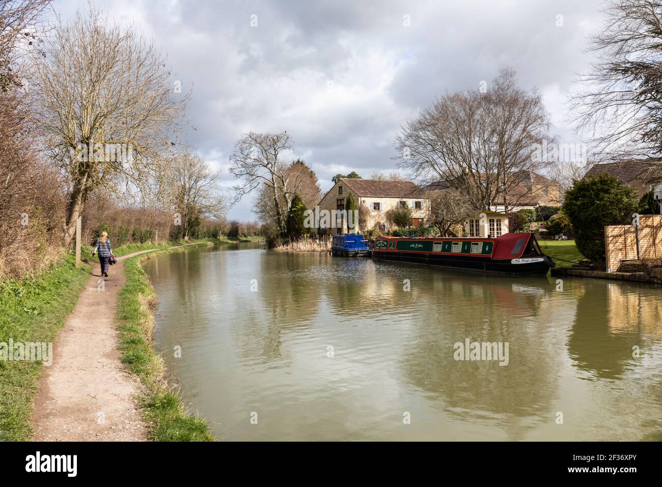 Donne che camminano lungo l'alzaia del canale Kennett e Avon a Hilperton con una barca canale e case accanto. Spring Trowbridge, Wiltshire, Regno Unito Foto Stock