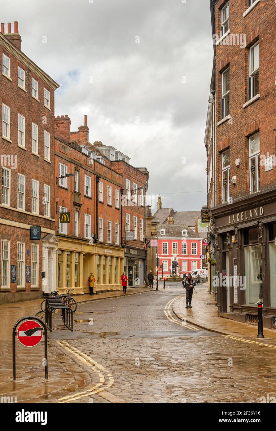 York Street dopo una doccia a pioggia. Gli edifici in mattoni rossi fiancheggiano la strada mentre si curva verso uno storico edificio rosso. Ci sono ciottoli nello straniero Foto Stock