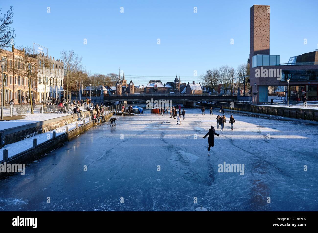 Amersfoort, Paesi Bassi - Feb 13, 2021: Persone pattinaggio su ghiaccio sul canale congelato l'EEM nel centro della città di Amersfoort con il famoso Koppelpoort nel Foto Stock