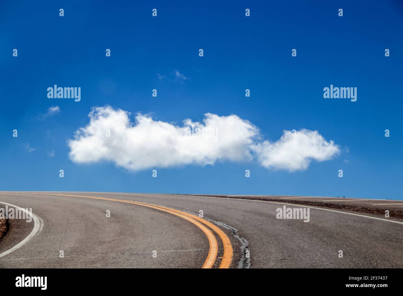 Strada al cielo - curva di strada in cima al nero con le strisce gialle si snoda intorno alla montagna e a tutto ciò che si può vedere è un cielo molto blu e una nuvola bianca soffice - pi Foto Stock