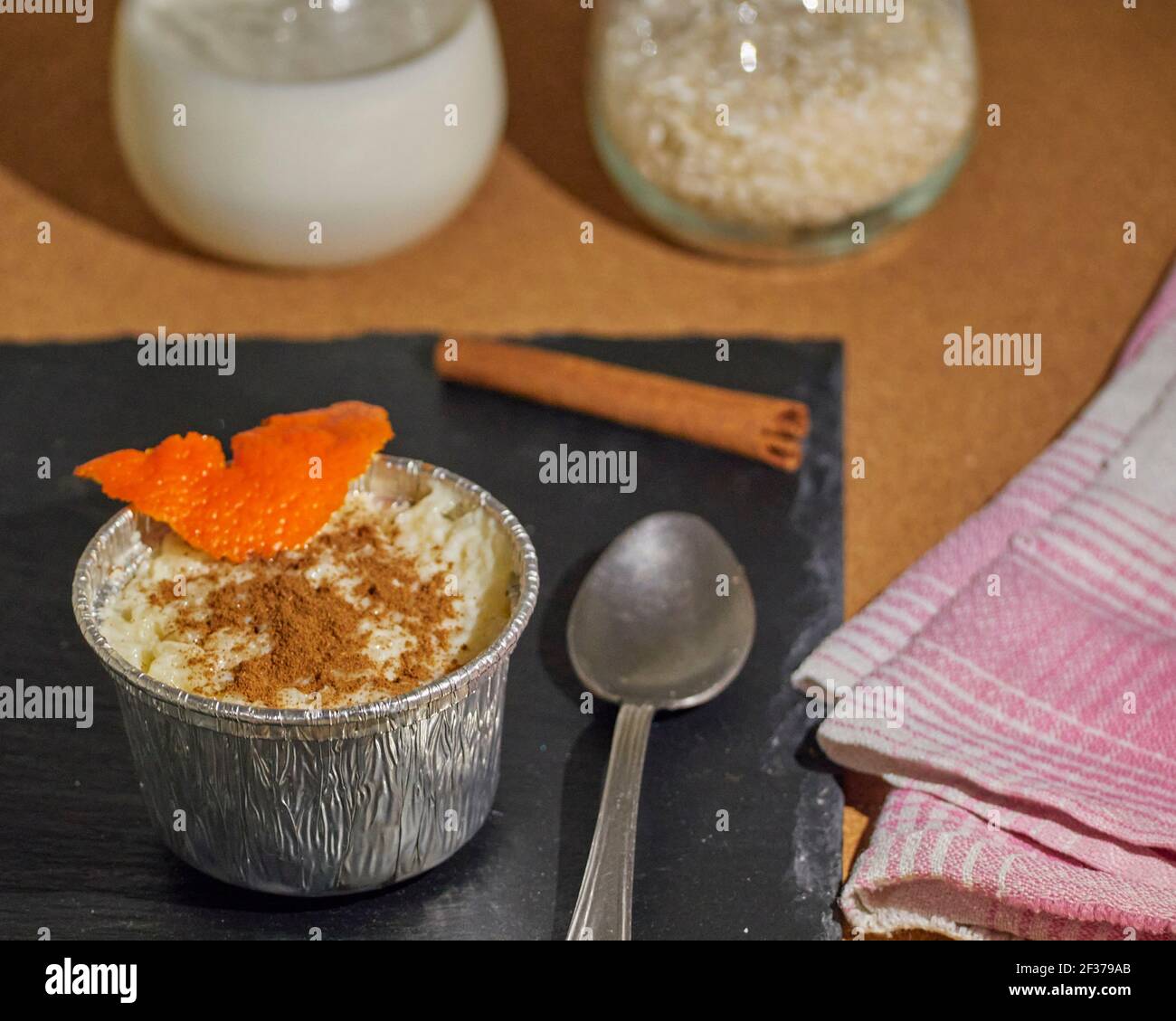 Budino di riso su tavola nera in ardesia decorata con bastone di cannella, un tovagliolo, una tazza di latte e una tazza di riso Foto Stock