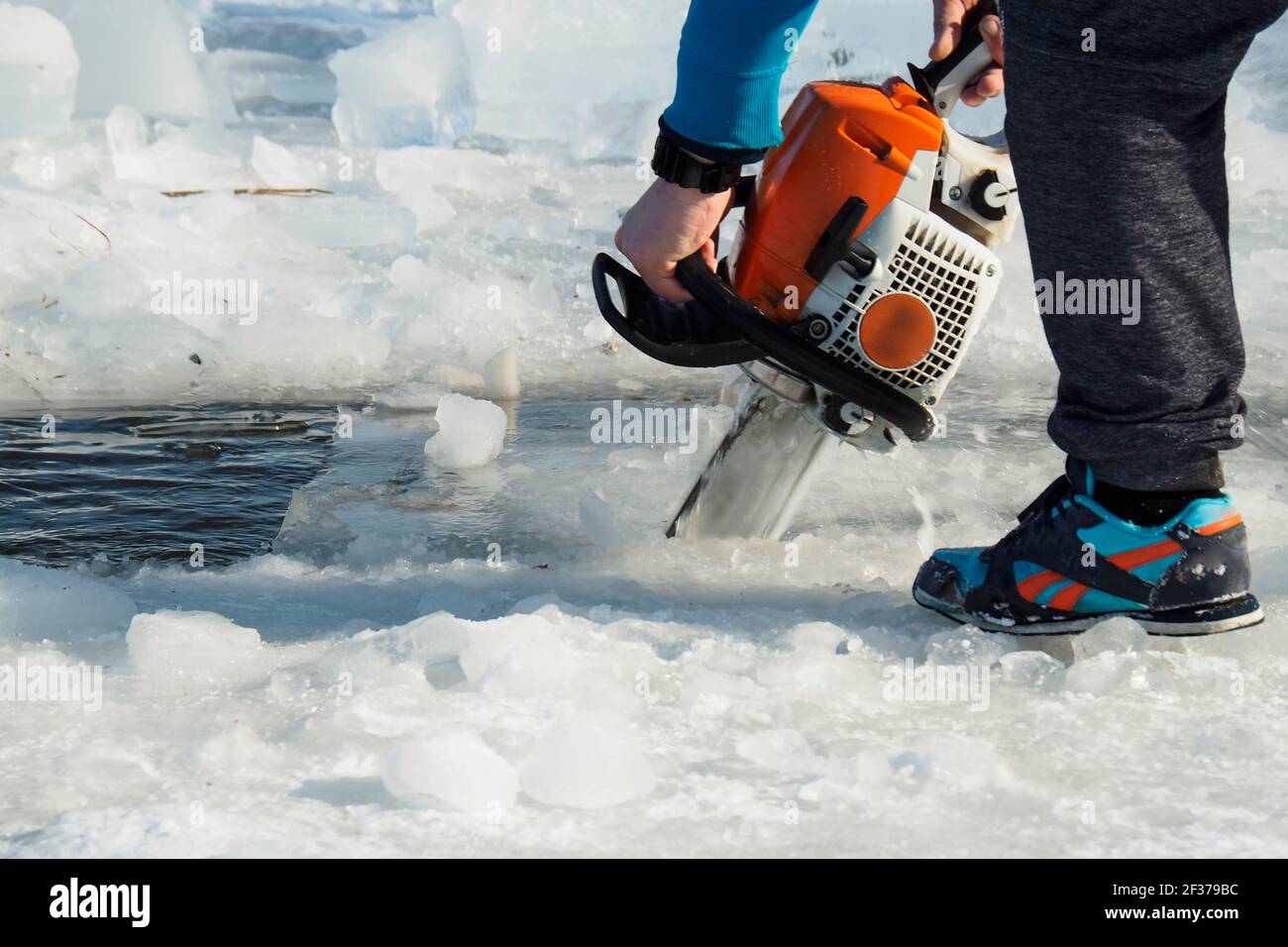 un uomo con una motosega taglia il ghiaccio sul lago Foto Stock