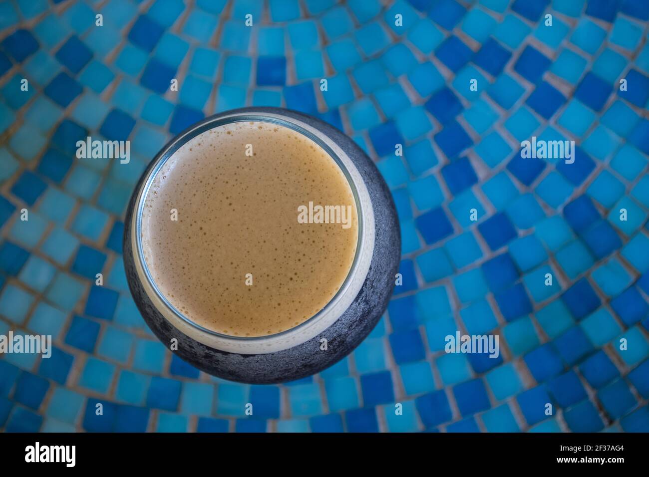Bicchiere rotondo di caffè freddo con parte superiore in schiuma seduta su un tavolo di tegole a mosaico blu in un caffè all'aperto' Foto Stock