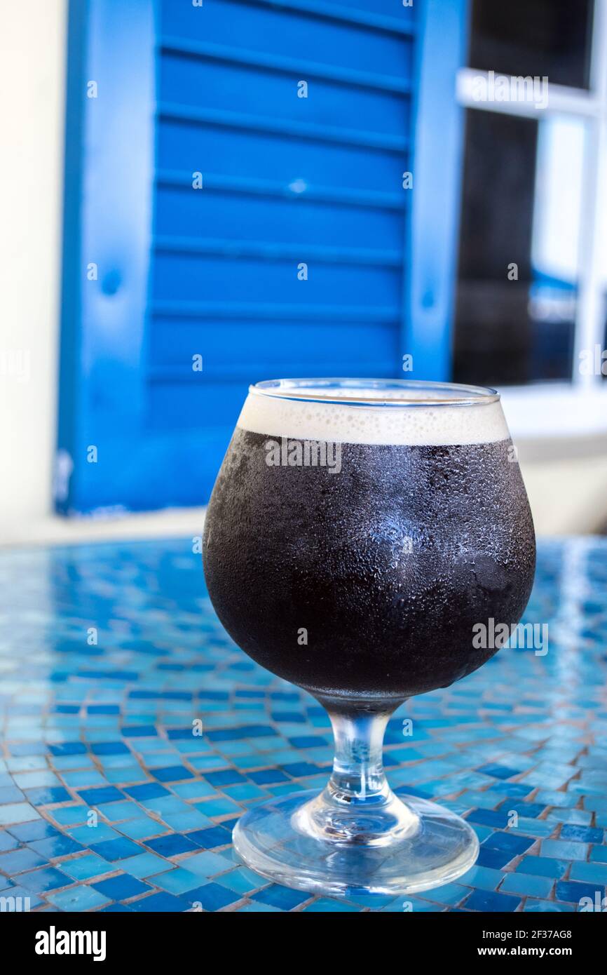 Bicchiere rotondo di caffè freddo con parte superiore in schiuma seduta su un tavolo di tegole a mosaico blu in un caffè all'aperto' Foto Stock