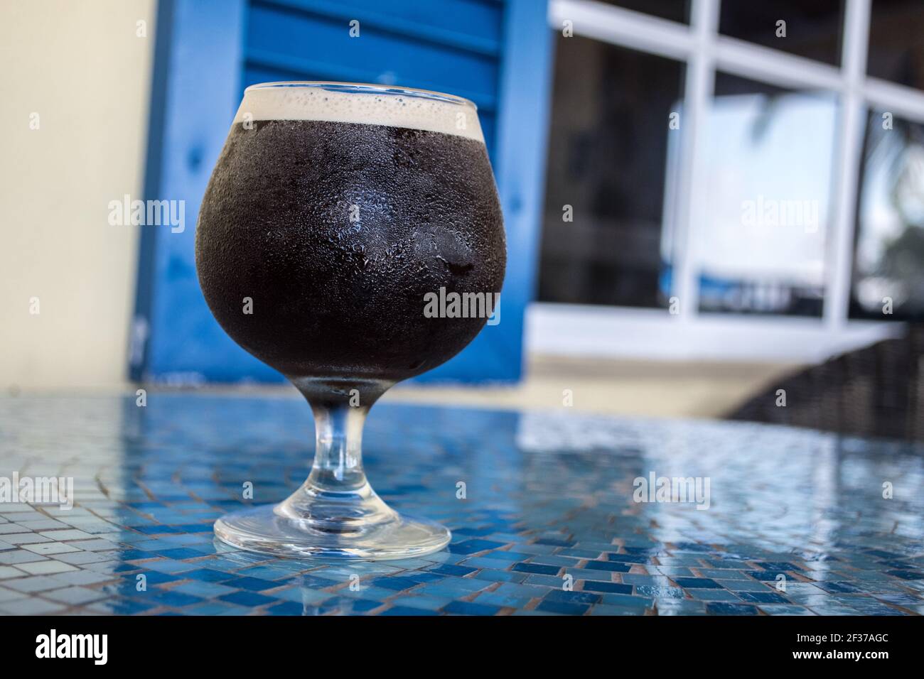 Bicchiere rotondo di caffè freddo con parte superiore in schiuma seduta su un tavolo di tegole a mosaico blu in un caffè all'aperto' Foto Stock