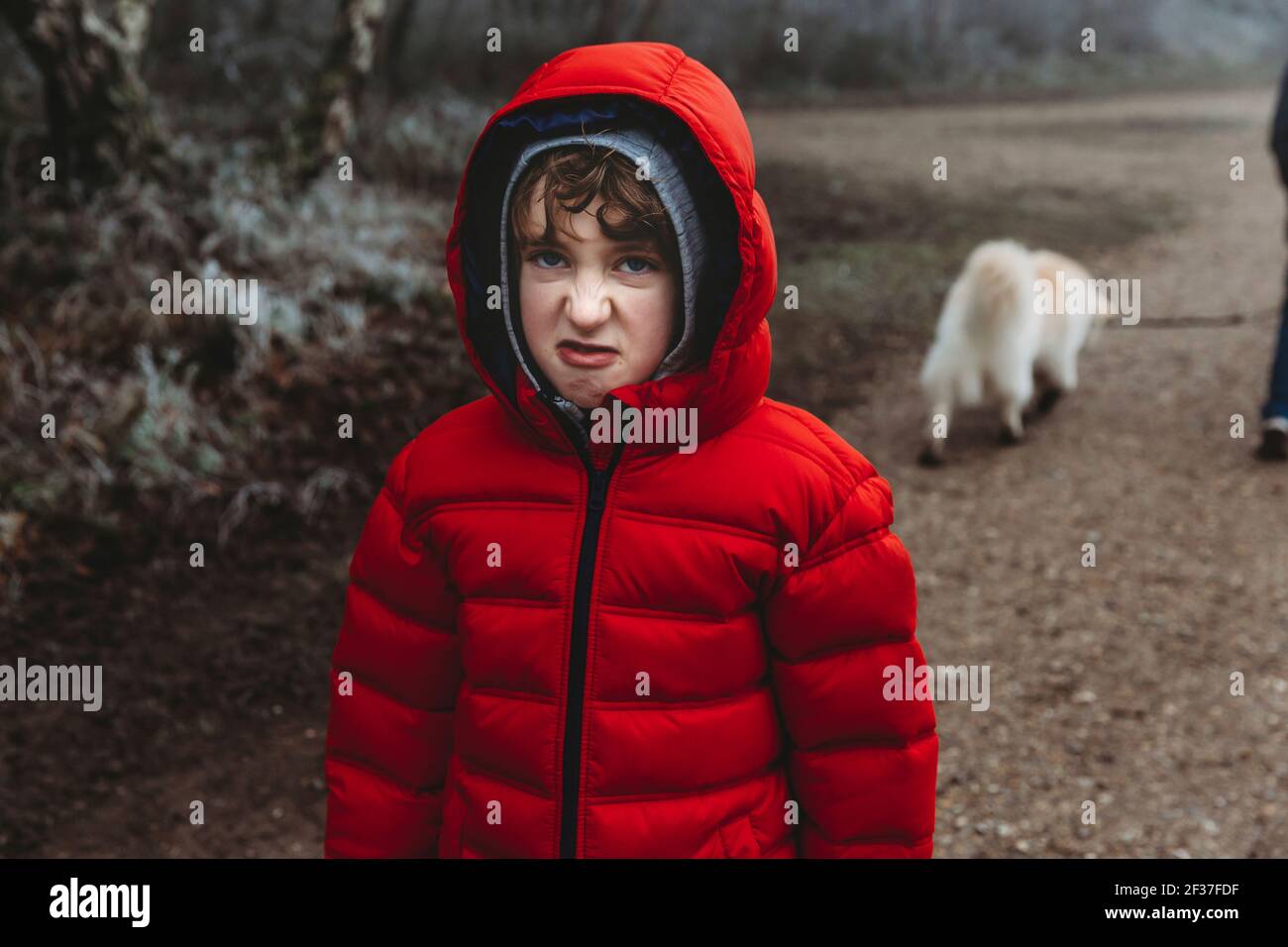 Ragazzo in cappotto rosso invernale guardando la macchina fotografica e serpente arricciarsi sul naso Foto Stock