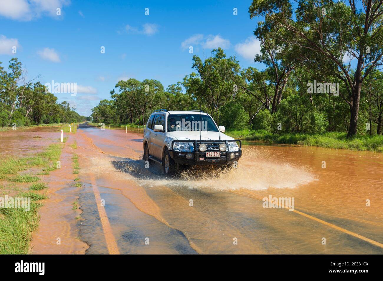 Un'auto che attraversa inondazioni su una remota strada Outback coperta di fango rosso dopo una tempesta, vicino a Thallon, Queensland, QLD, Australia Foto Stock