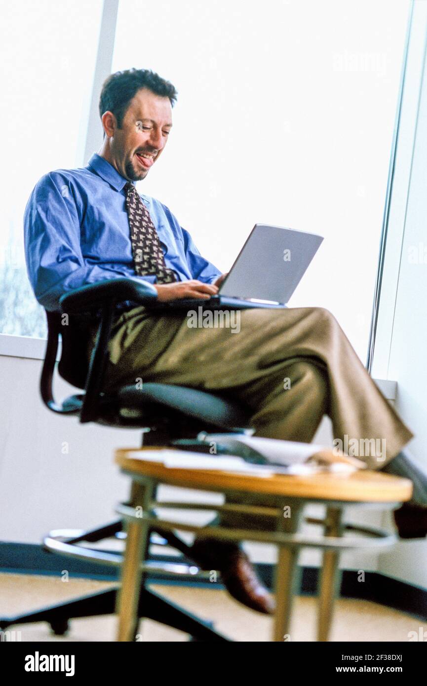 Uomo d'affari che ride mentre lavora su un computer portatile. Foto Stock