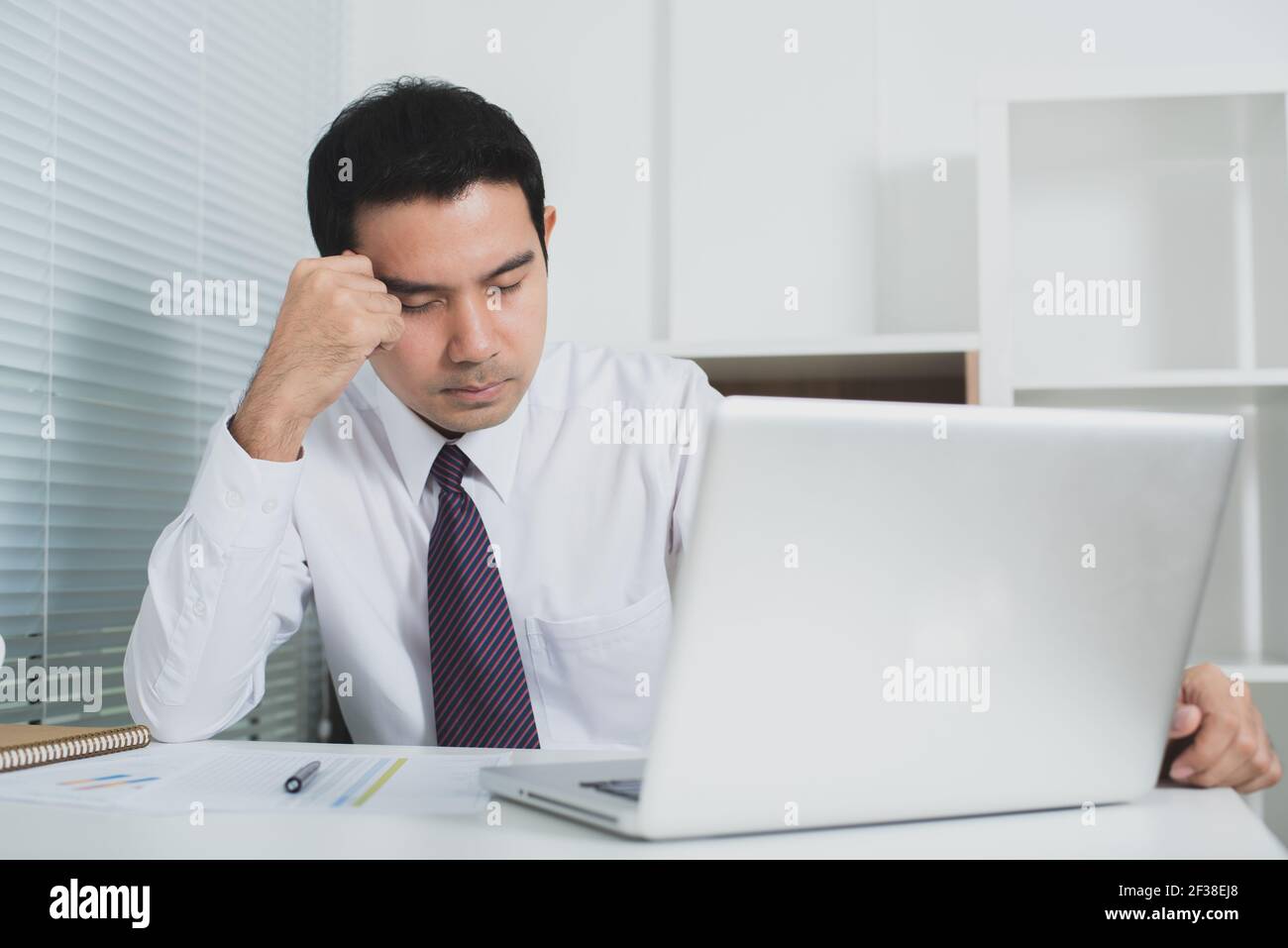 Uomo d'affari asiatico sempre stressato al lavoro di fronte al portatile computer - segnale acustico Foto Stock