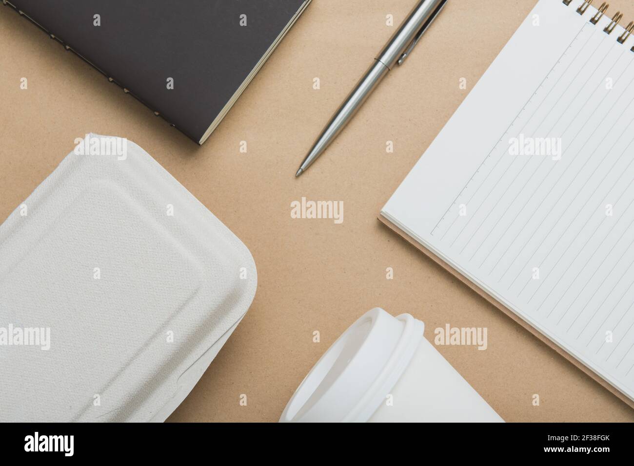 Taccuini, penna, tazzina da asporto e scatola di cibo su carta marrone - disposizione piatta (vista dall'alto) Foto Stock
