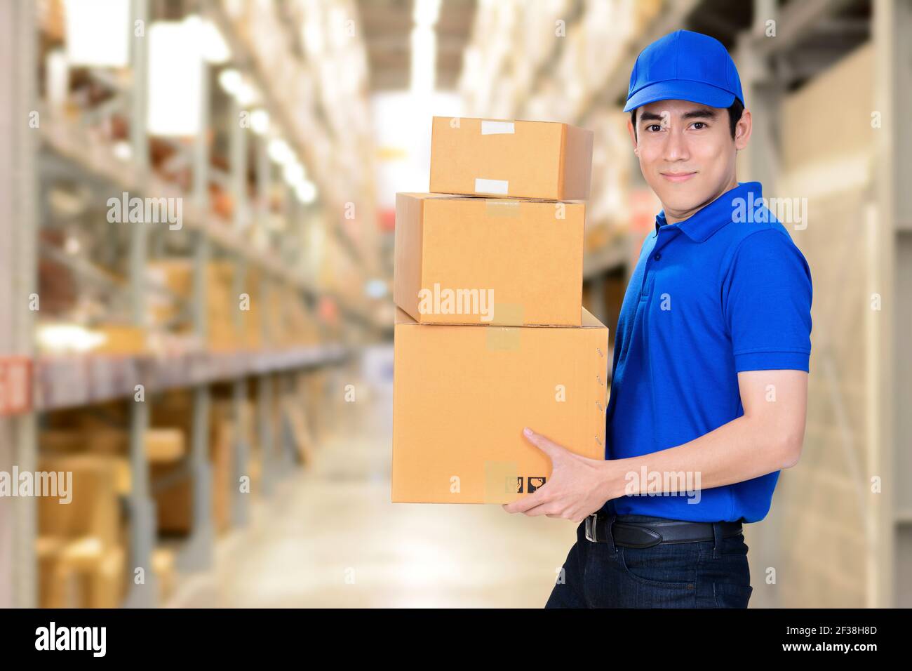 Sorridente addetto alla consegna che porta scatole su sfondo di magazzino sfocato Foto Stock