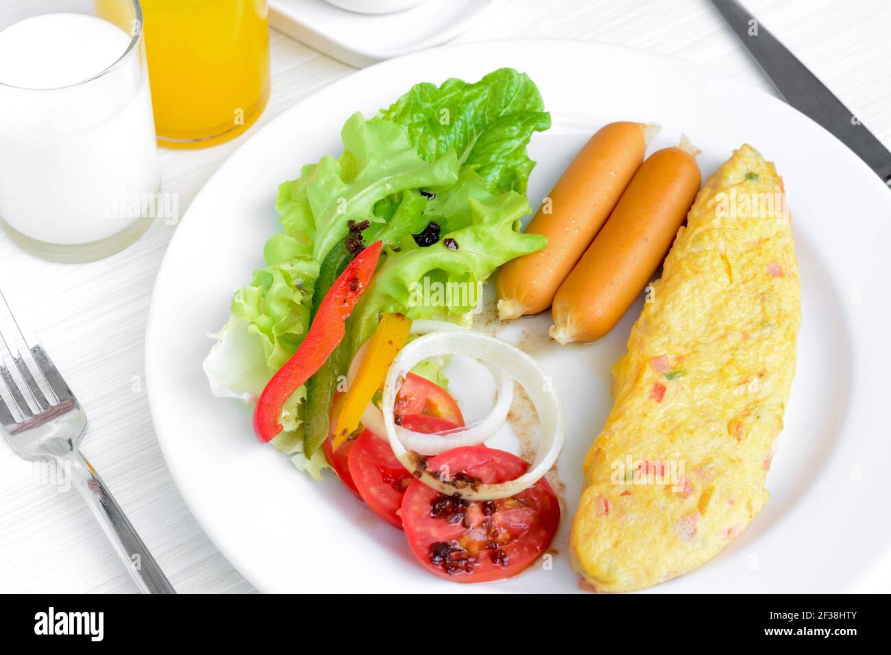 La colazione include omelette, salsiccia, latte, succo di frutta e insalata colorata con condimento italiano Foto Stock