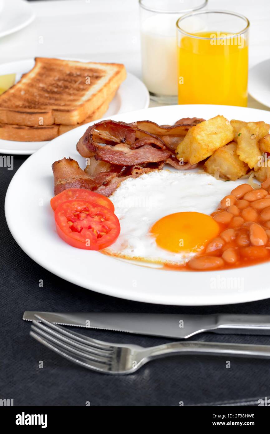 Colazione all'inglese, con uova fritte, fagioli al forno, patate, pancetta, un po' di pane, succo di frutta e latte Foto Stock