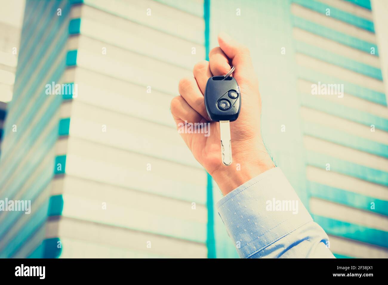 Mano che tiene la chiave di automobile sullo sfondo dell'edificio, tono vintage Foto Stock