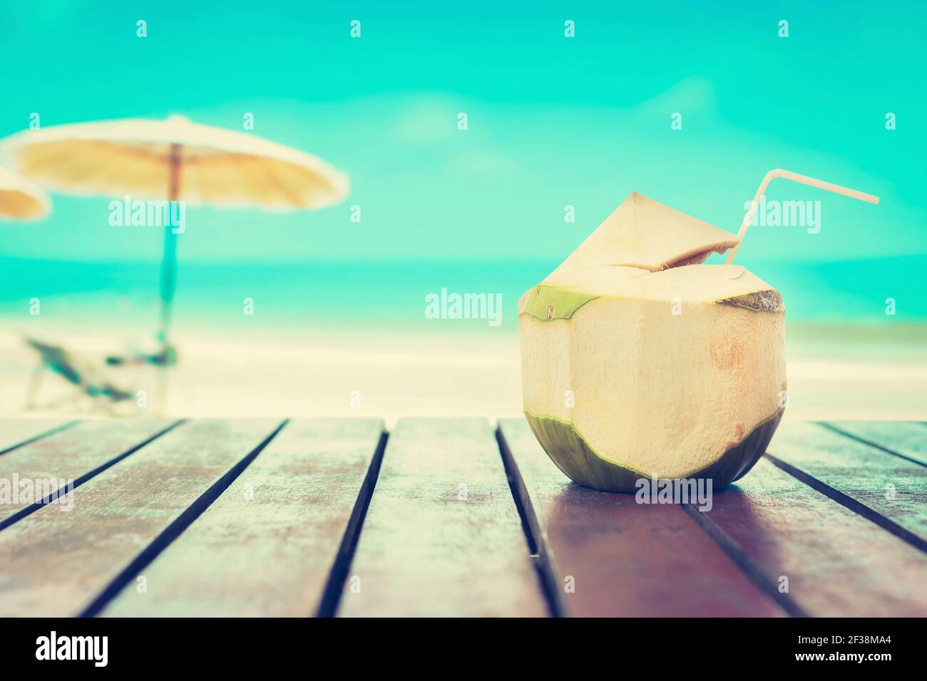 Succo di cocco su tavolo di legno sullo sfondo della spiaggia offuscata - concetto di vacanza estiva, tonalità vintage Foto Stock