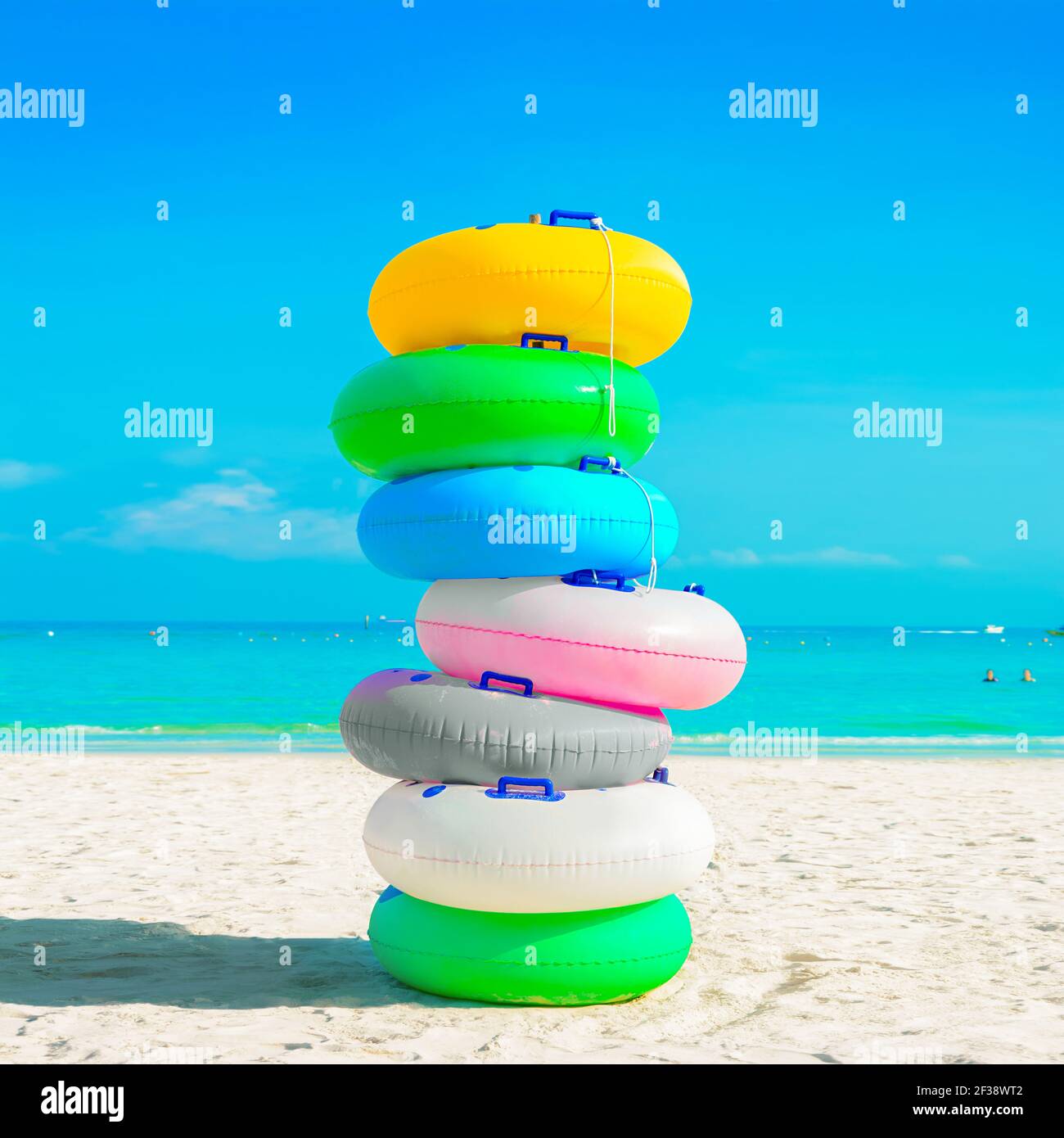 Pila di anelli colorati in gomma (o anelli da nuoto) sulla spiaggia di sabbia bianca - concetto di vacanza estiva Foto Stock