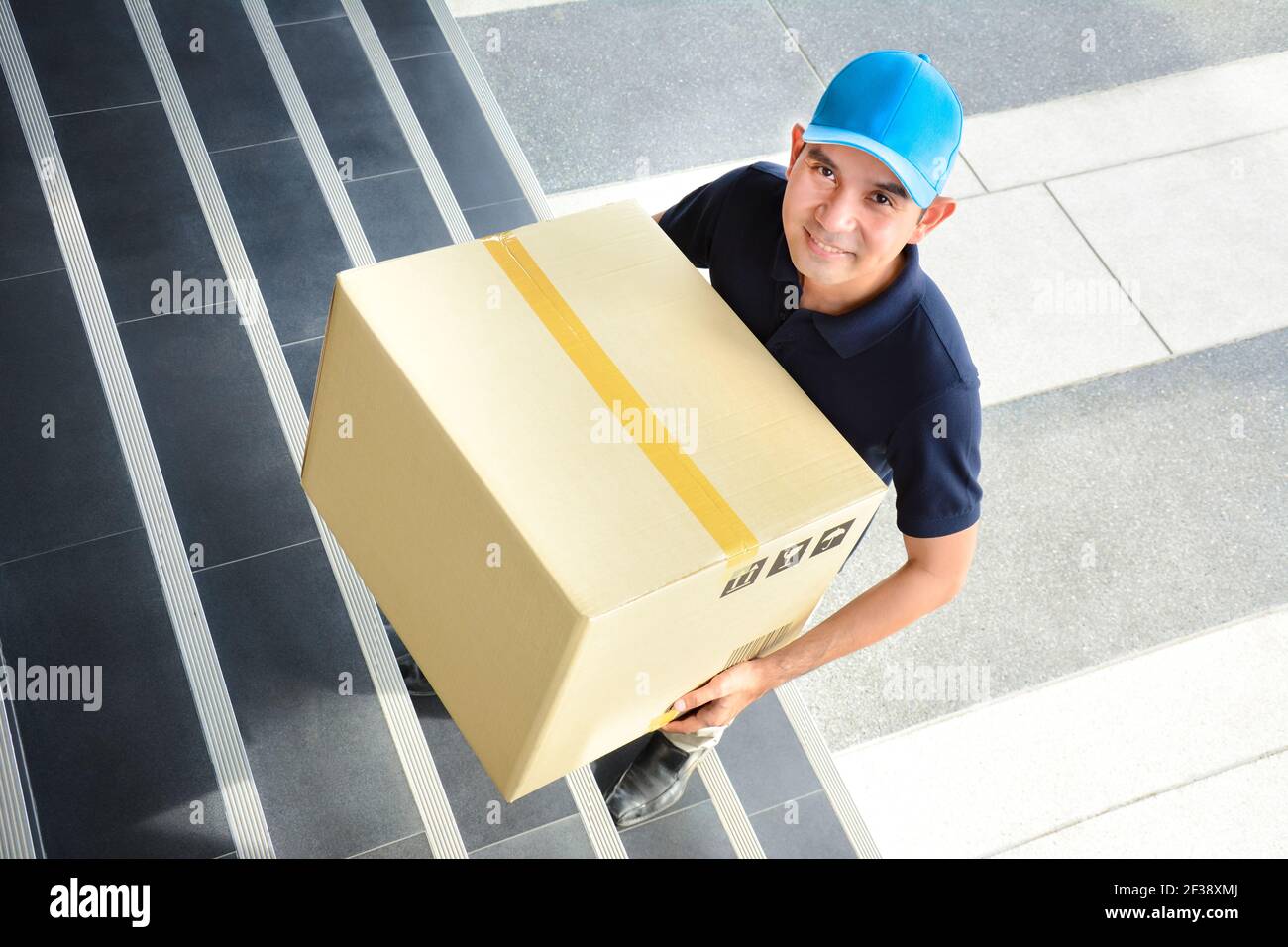 Il deliveryman salendo le scale, trasportando una grande scatola di pacchi Foto Stock