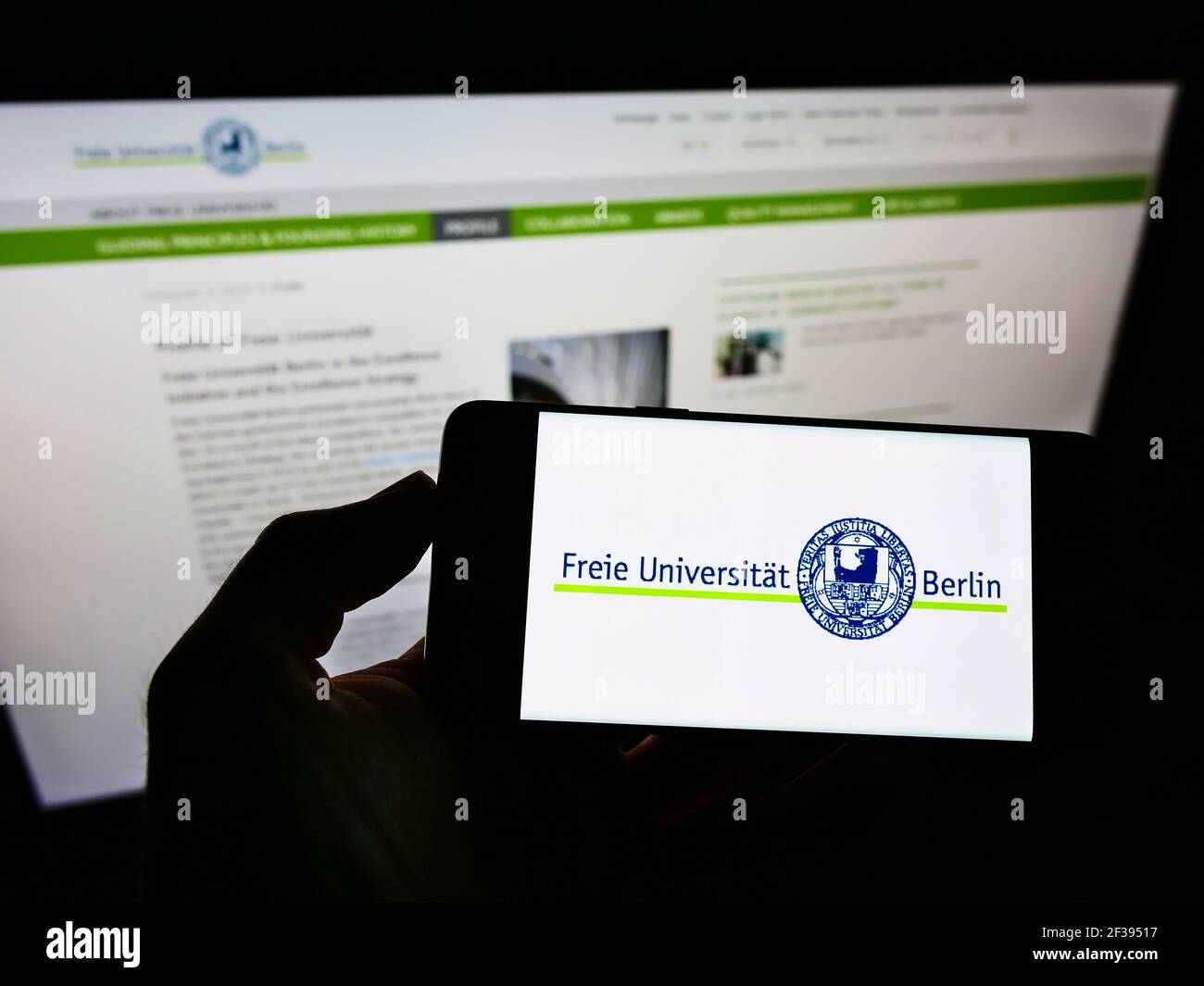 Persona in possesso di smartphone con logo dell'università tedesca Freie Universität Berlin (fu) sullo schermo di fronte al sito Web. Mettere a fuoco il display del telefono. Foto Stock