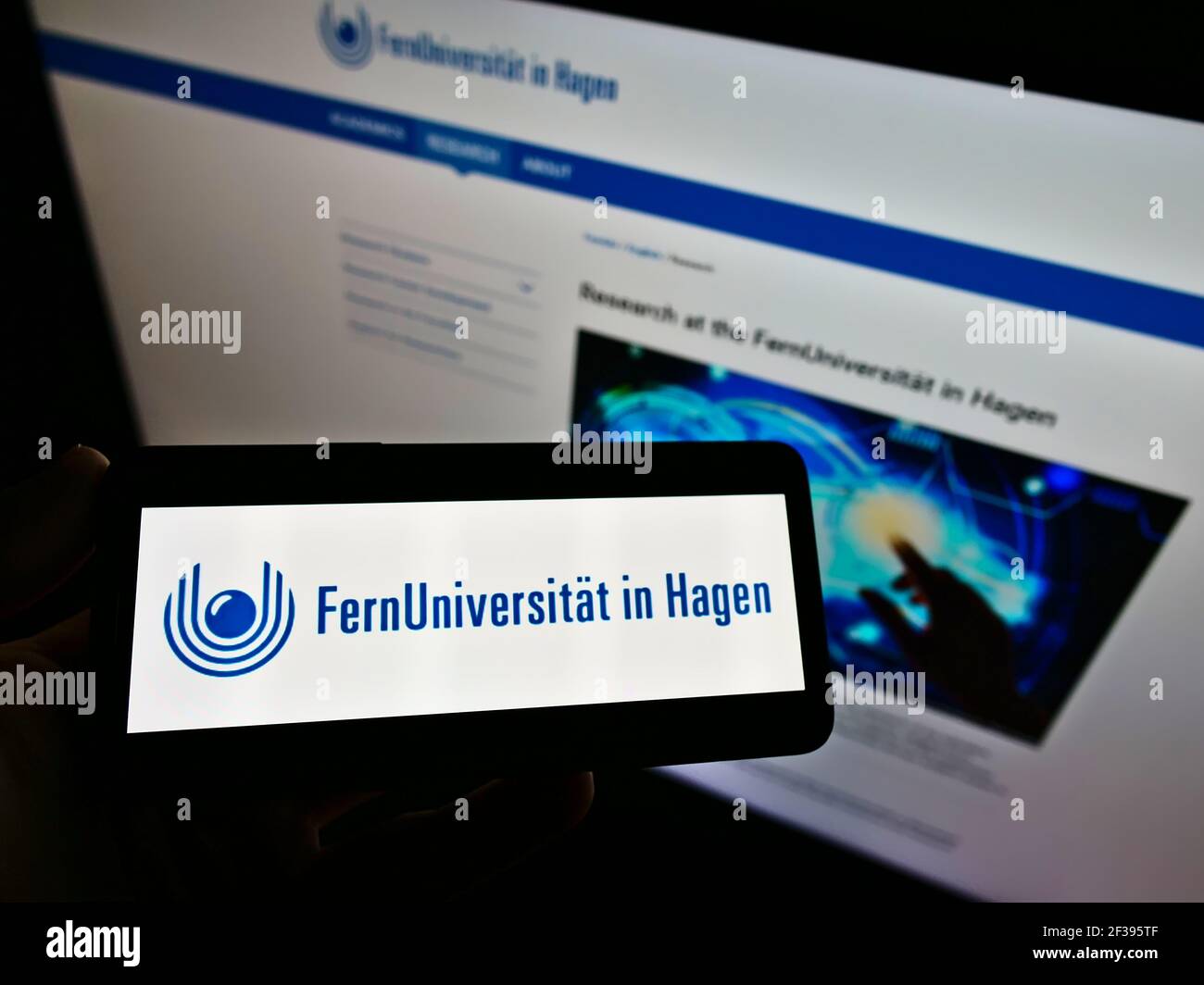 Persona che tiene il cellulare con il logo dell'istituto tedesco di istruzione Università di Hagen sullo schermo di fronte alla pagina web. Mettere a fuoco il display del telefono. Foto Stock