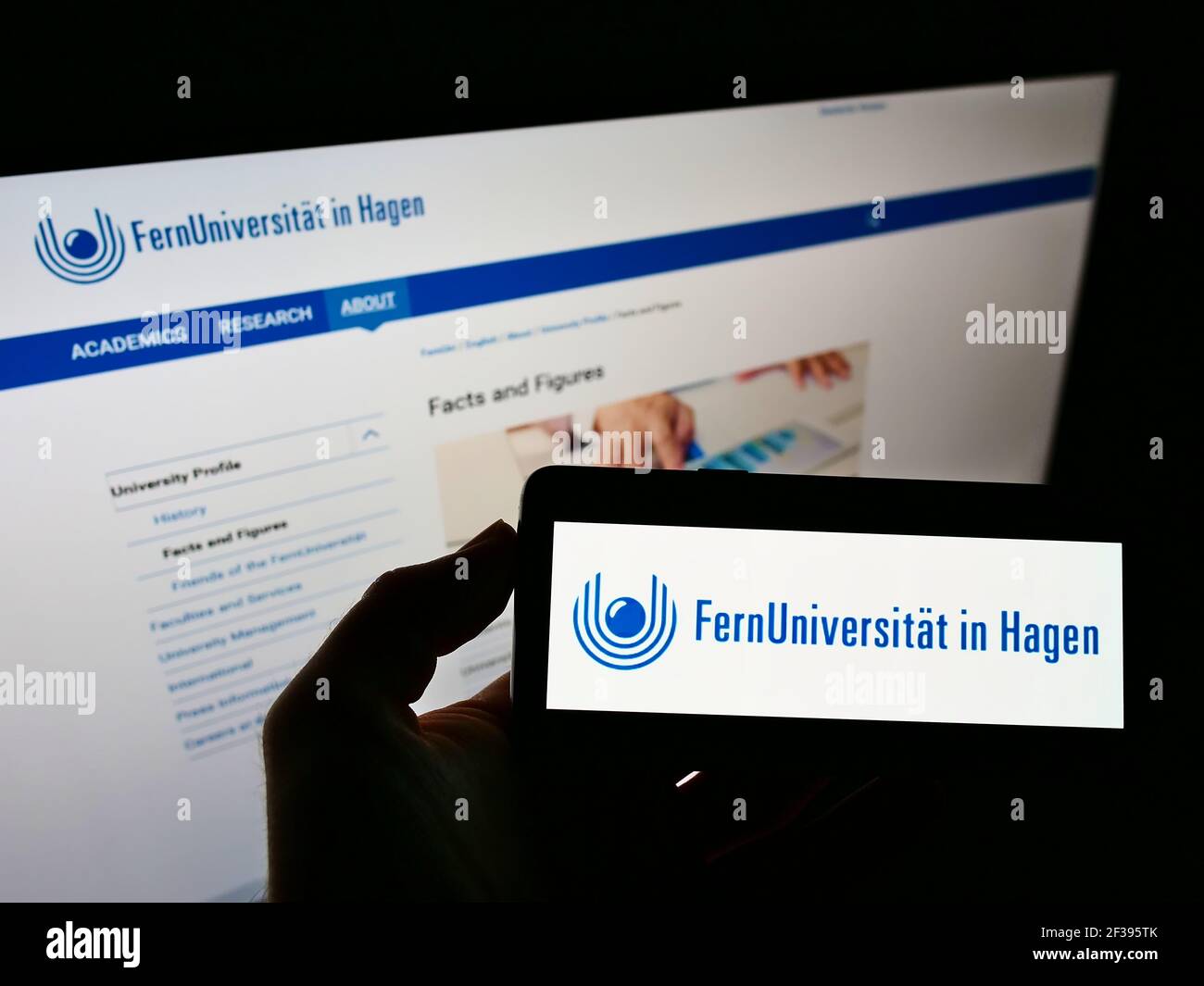 Persona che detiene smartphone con il logo dell'università tedesca FernUniversität a Hagen sullo schermo di fronte al sito web. Mettere a fuoco il display del telefono. Foto Stock