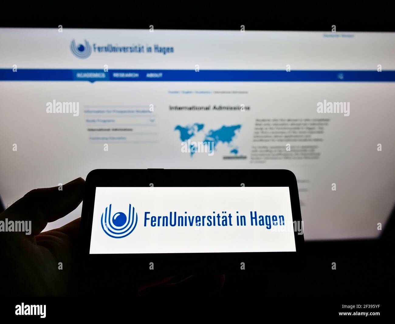 Persona che detiene il cellulare con il logo dell'università tedesca FernUniversität a Hagen sullo schermo davanti alla pagina web. Focus sul display del cellulare. Foto Stock