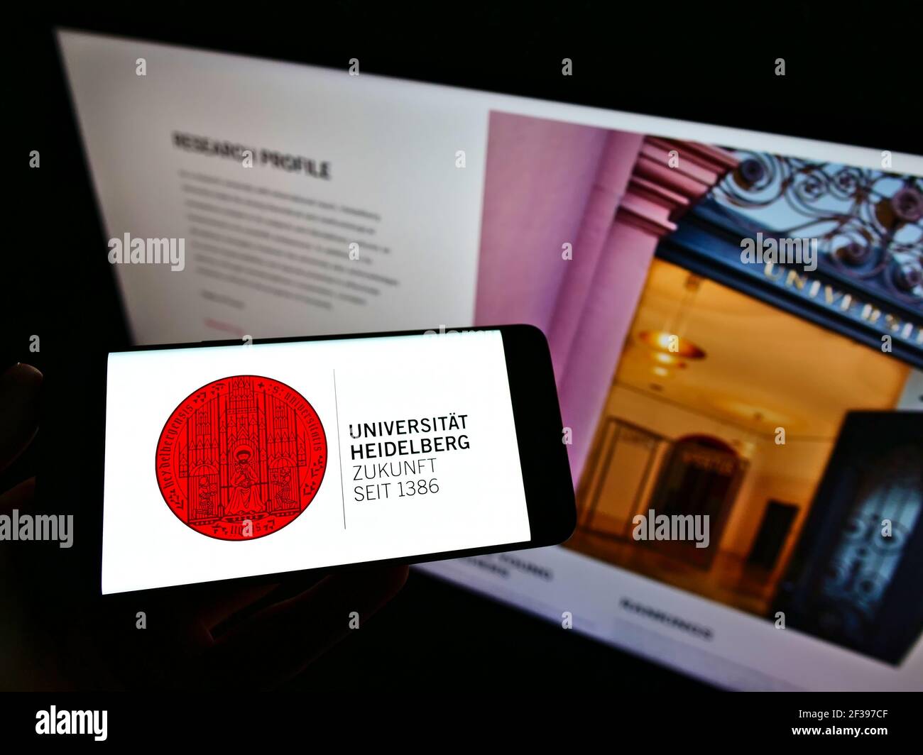Persona che detiene smartphone con il logo dell'università tedesca Ruprecht-Karls-Universität Heidelberg sullo schermo davanti al sito web. Mettere a fuoco il display del telefono. Foto Stock