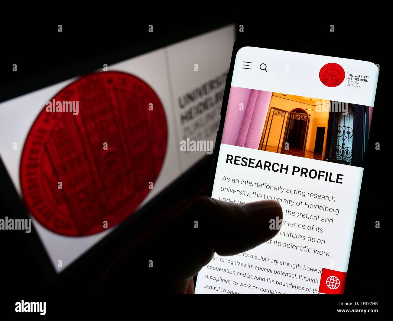 Persona che tiene il cellulare con la pagina web dell'Università tedesca di Heidelberg sullo schermo davanti al logo. Mettere a fuoco il centro del display del telefono. Foto non modificata. Foto Stock