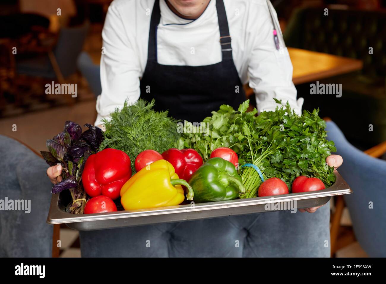 Alto angolo di raccolto irriconoscibile chef in grembiule con in piedi vassoio pieno di varie verdure fresche ed erbe Foto Stock