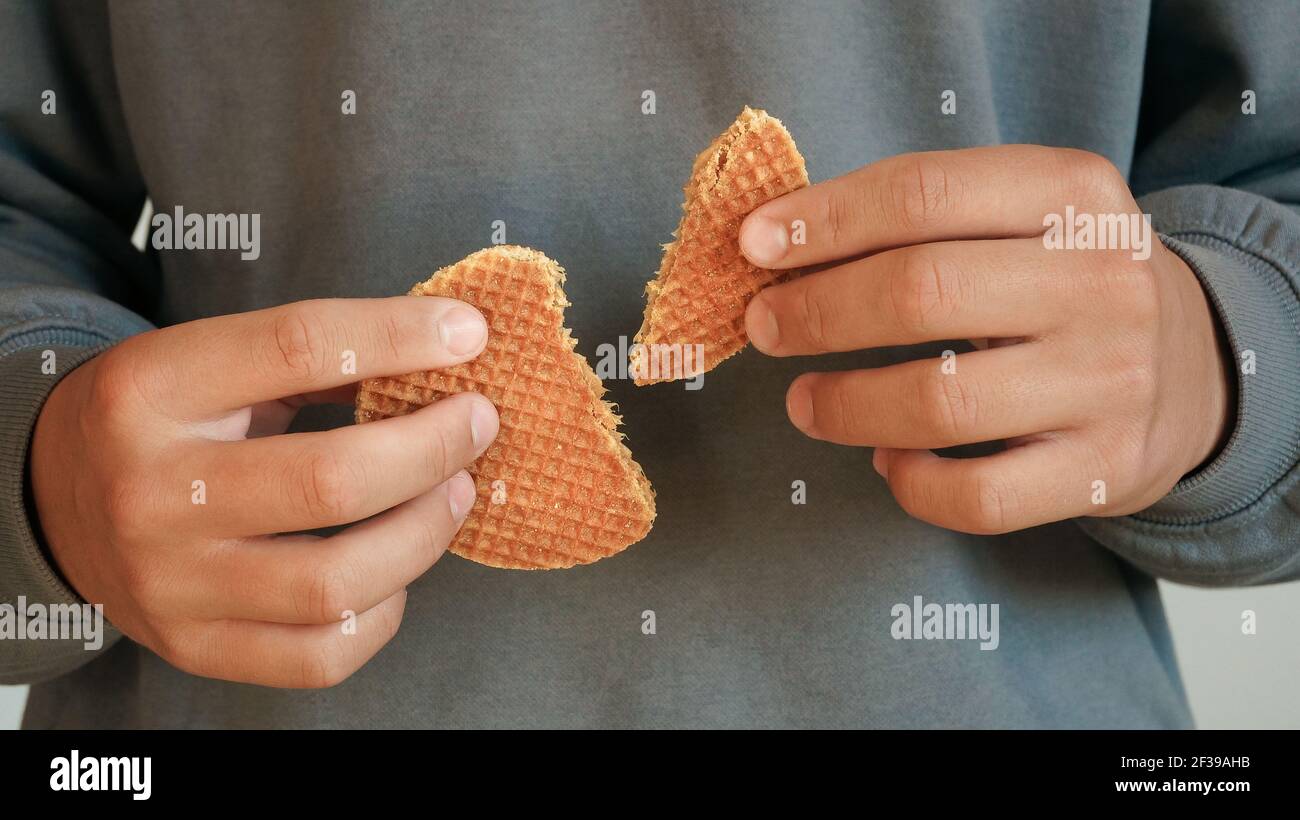 Giovane uomo che tiene due metà olandese caramello waffle tradizionale fatto a mano sfondo felpa grigio dessert Foto Stock