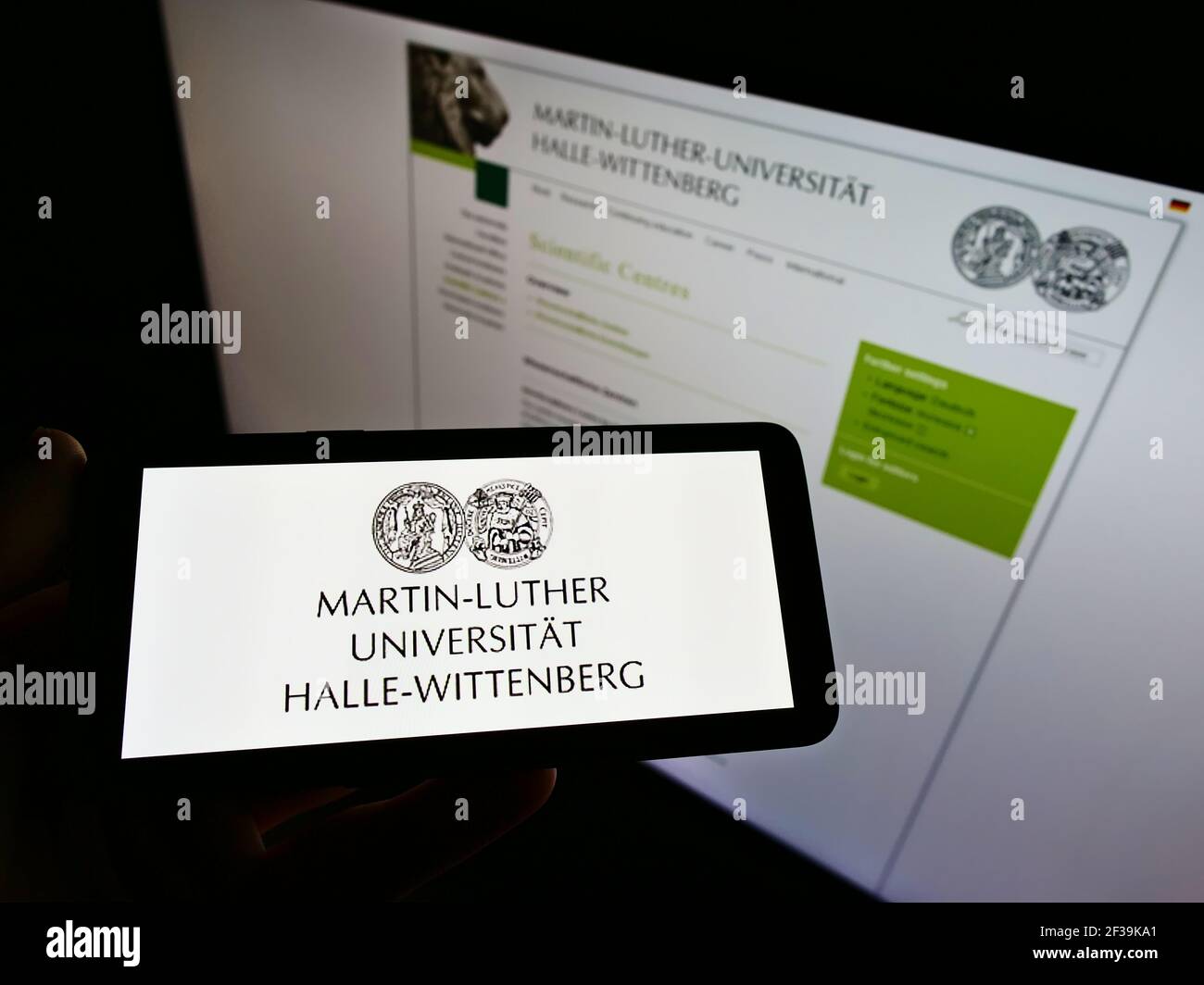 Persona che tiene il cellulare con il logo della tedesca Martin Luther University di Halle-Wittenberg sullo schermo di fronte alla pagina web. Mettere a fuoco il display del telefono. Foto Stock