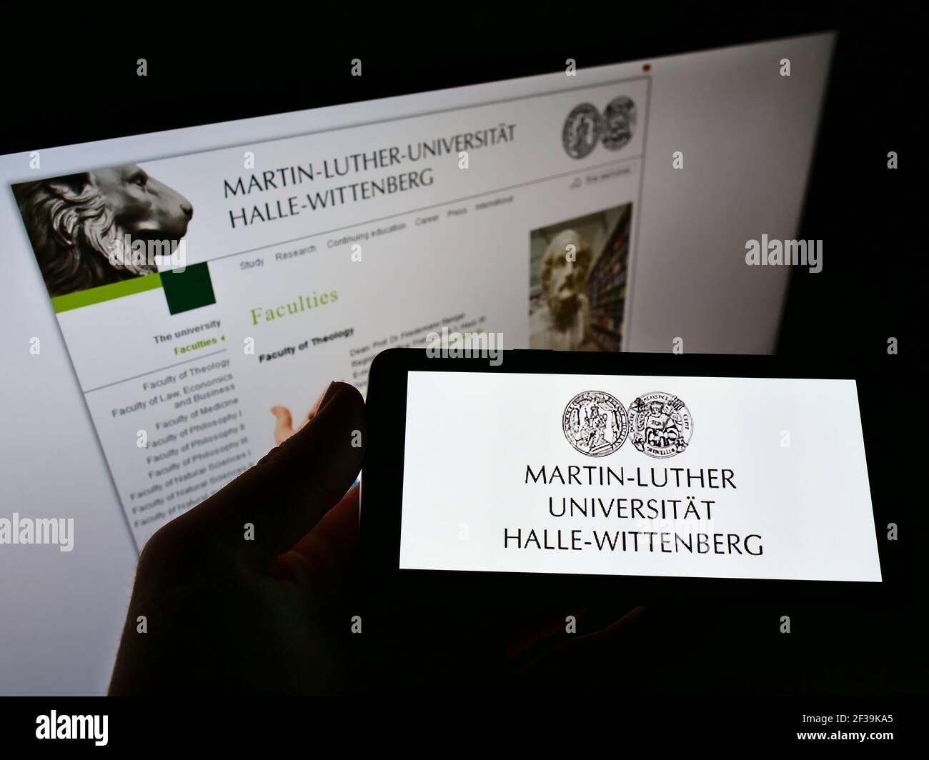 Persona che detiene il cellulare con il logo tedesco Martin-Luther-Universität Halle-Wittenberg sullo schermo davanti alla pagina web. Mettere a fuoco il display del telefono. Foto Stock