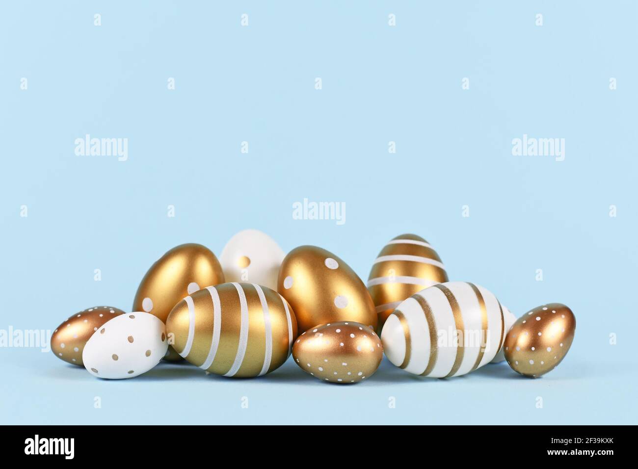 Eleganti uova di Pasqua dorate e bianche dipinte con semplici puntini e strisce su sfondo blu Foto Stock