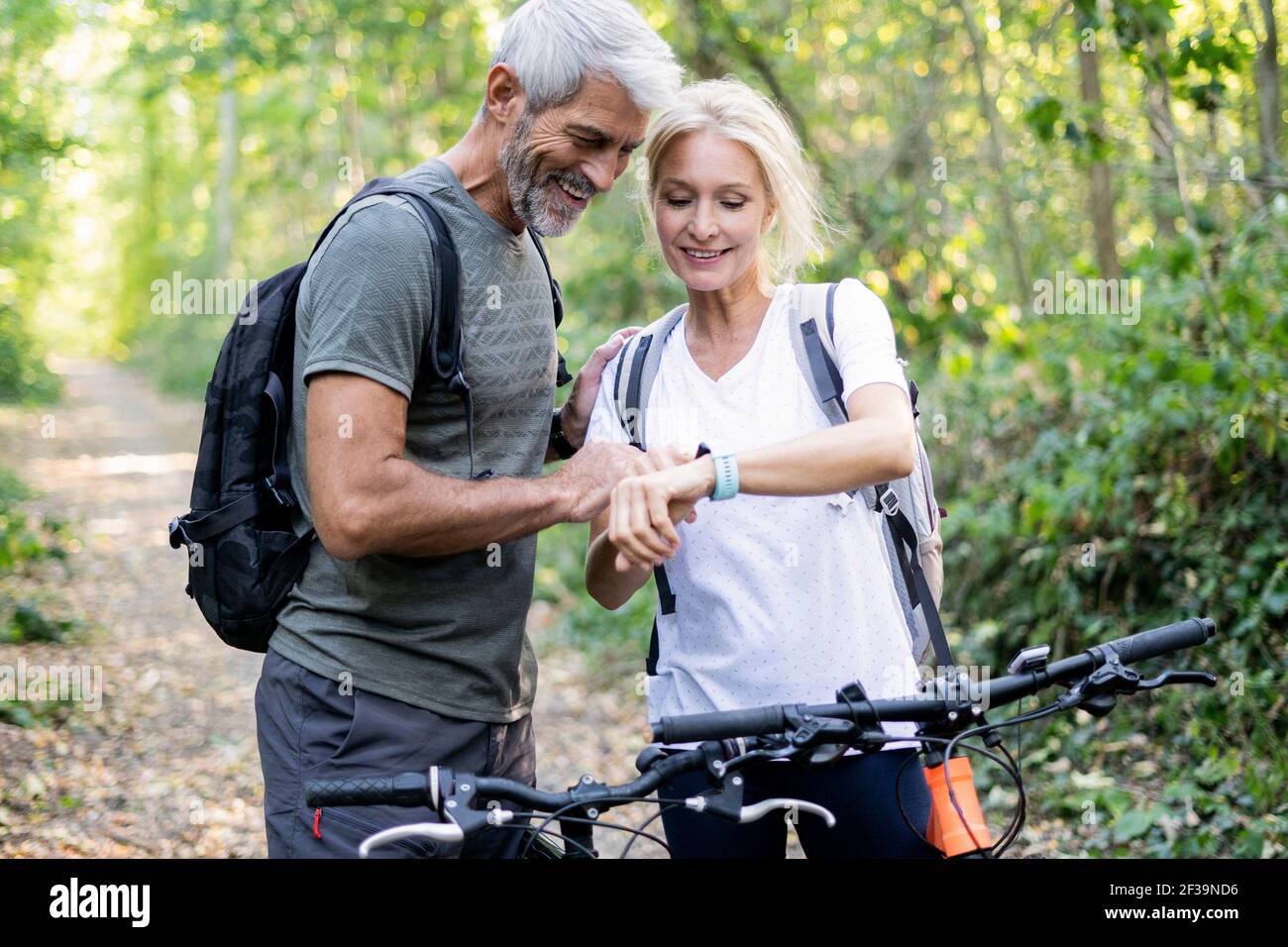 Sorridente coppia matura controllo direzione su smart watch in foresta Foto Stock