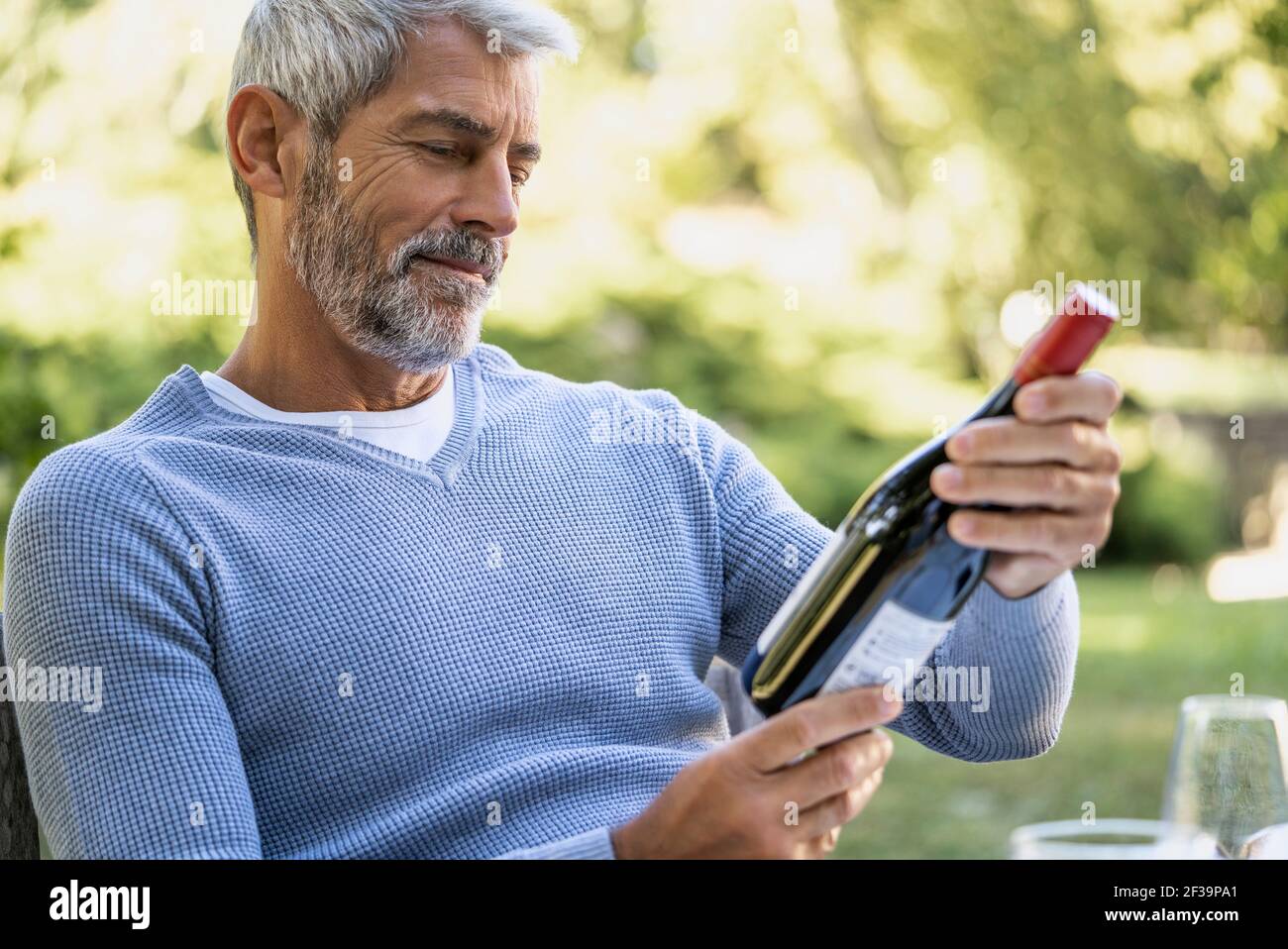 Uomo maturo che guarda la bottiglia di vino mentre si siede sulla sedia Foto Stock