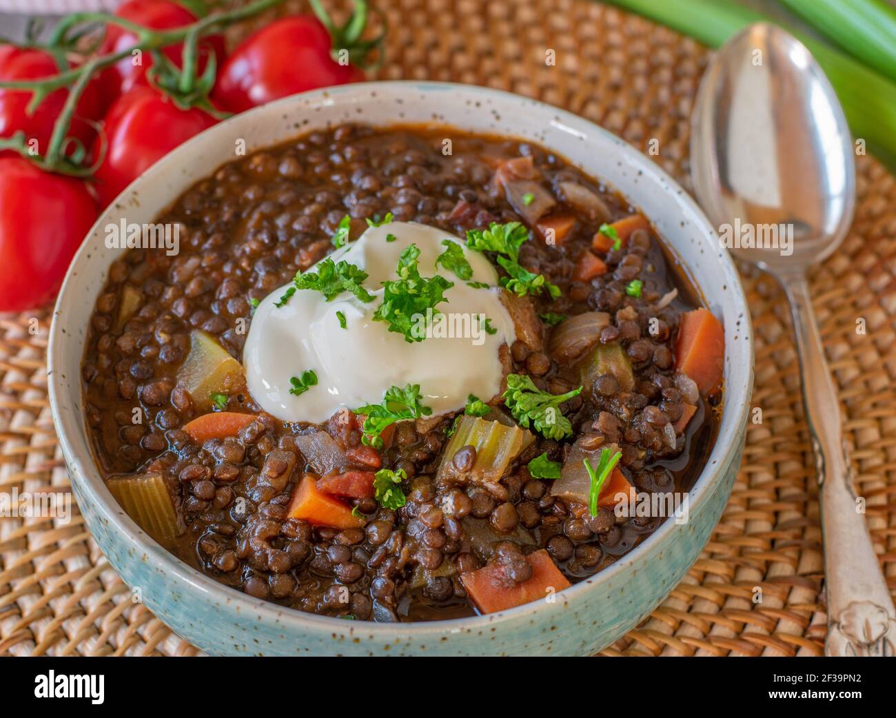 Stufate con lenticchie beluga, verdure e crema acida servita in una ciotola dall'alto con cucchiaio Foto Stock