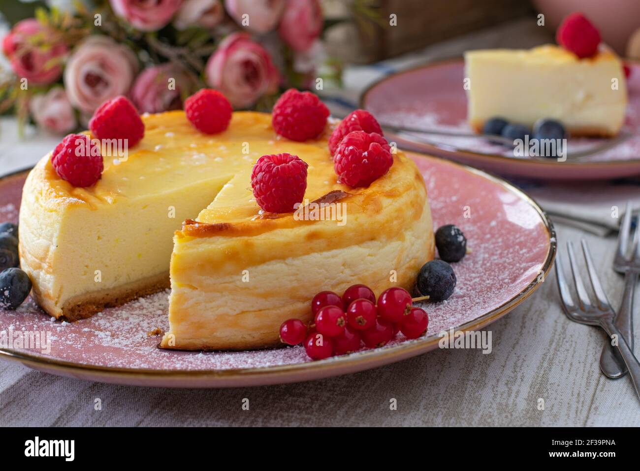 tavolo in rosa pallido con cheesecake, fiori e forchette Foto Stock