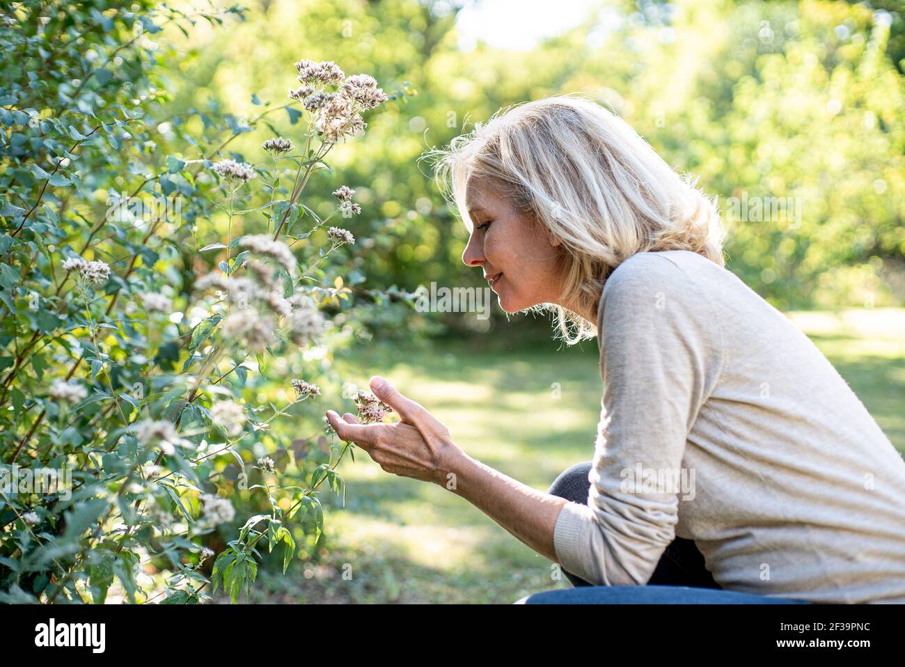 Donna matura sorridente che guarda i fiori nel cortile Foto Stock