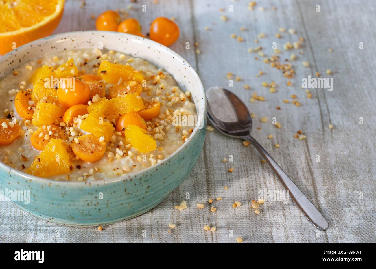 Colazione porridge di farinata d'avena con arance e fisalis servita con arrosto noci in una ciotola su un tavolo di legno chiaro con spazio di copia Foto Stock