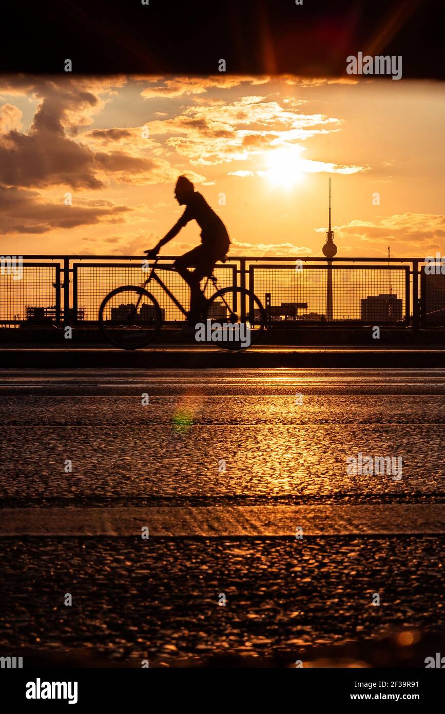 Silhouette di uomo in bicicletta sul ponte con Fernsehturm Berlino sullo sfondo durante il tramonto Foto Stock