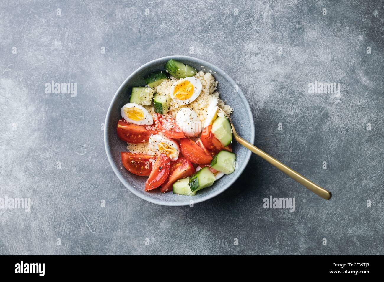 Ciotola per insalata di cous cous vegano con cetriolo, pomodori ciliegini e uova di quaglia su un tavolo di pietra. Vista dall'alto. Insalata semplice con ingredienti minimi. Foto Stock