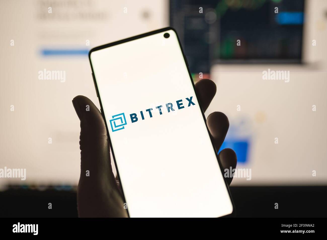 Uomo che tiene uno smartphone con il logo Bittrex con sito web sfocato come sfondo. Scambio di criptovaluta, piattaforma di trading Foto Stock